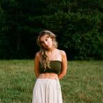 Sydney Rose in a field of grass, she is wearing a green bralette and white pants